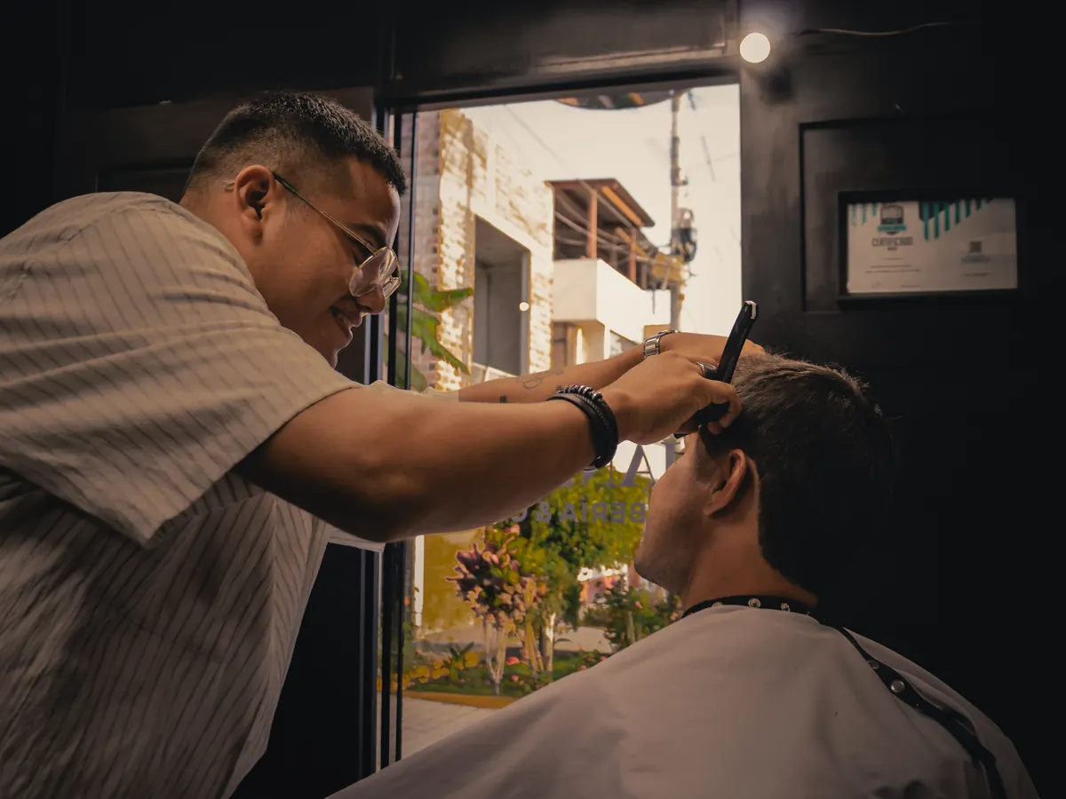 Gianpiert sonriendo mientras corta el cabello a un cliente